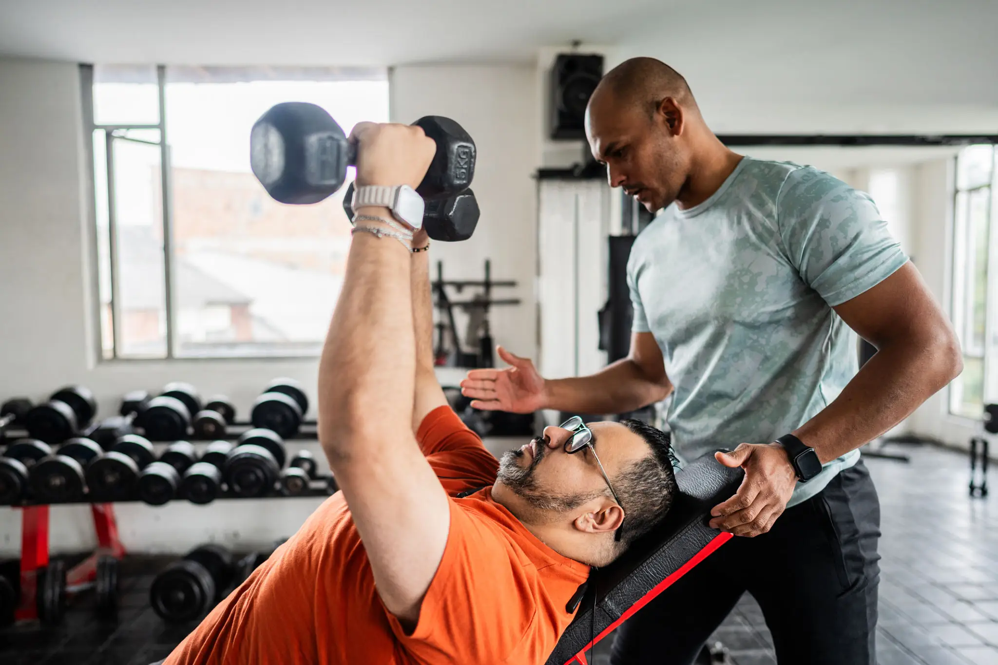 Man lifting weights with trainer's assistance.
